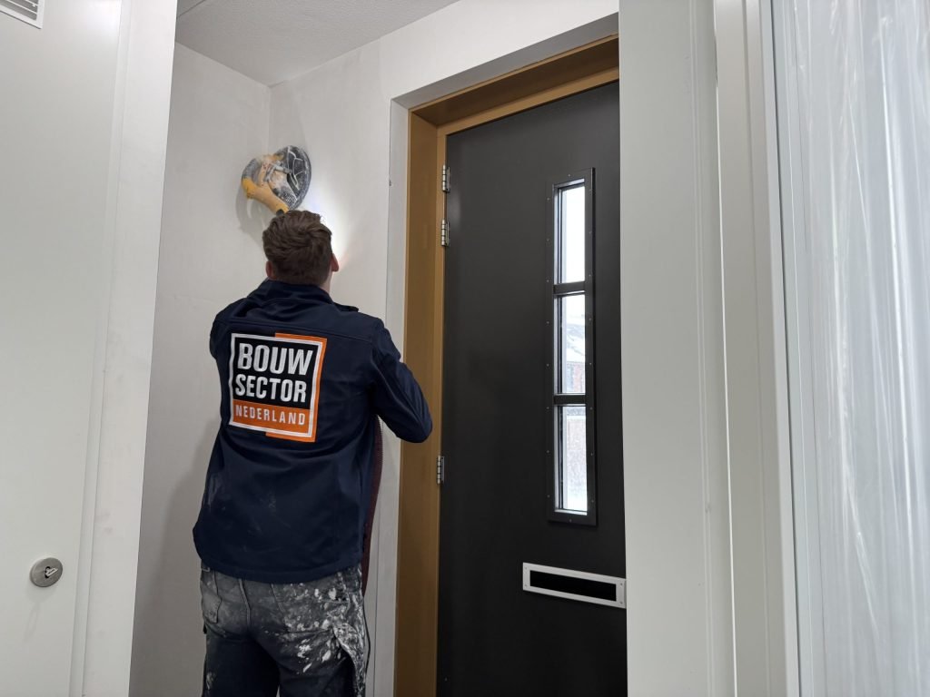 Vakman van Bouwsector Nederland schuurt een wand en plafondhoek met een schuurmachine