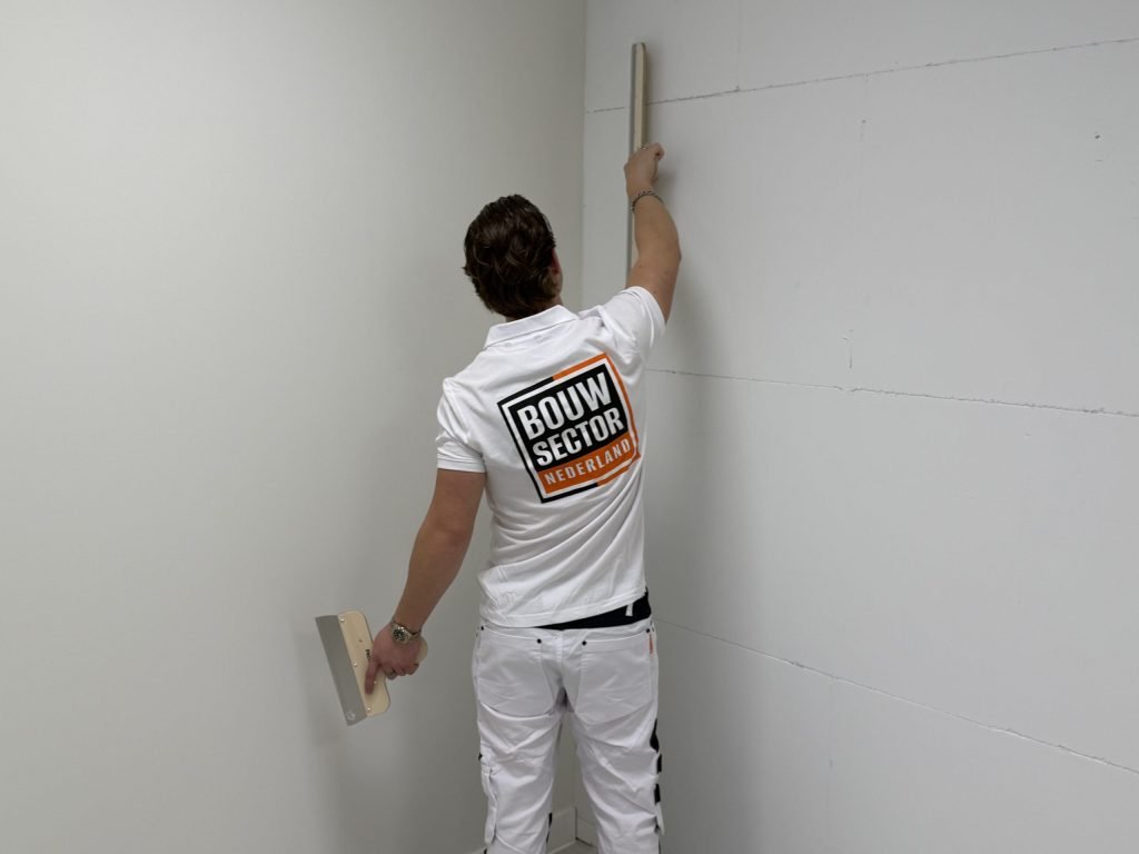 Stukadoor controleert met een rei of de wand vlak is, met de spaan in de hand